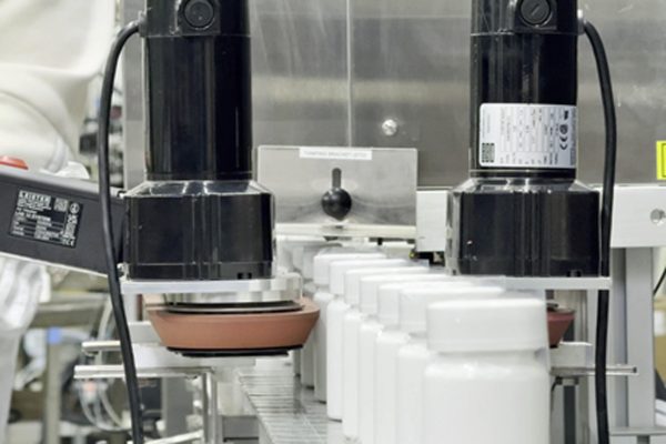 Pharmafill NB1 with bottomless conveyor applying tamper-evident bands onto white plastic bottles